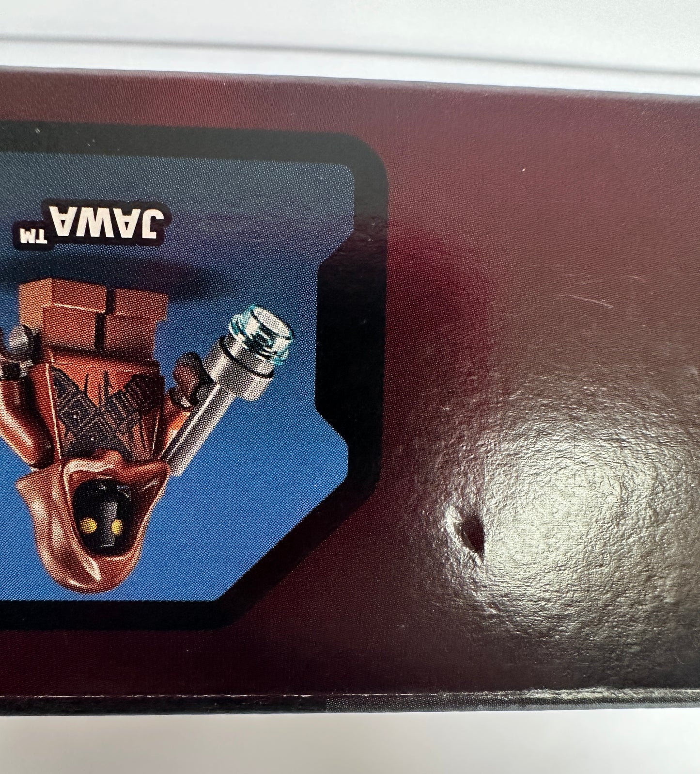 Small figurine of a character from 'Star Wars' on a card with 'Jawa' branding, attached to a dark surface.